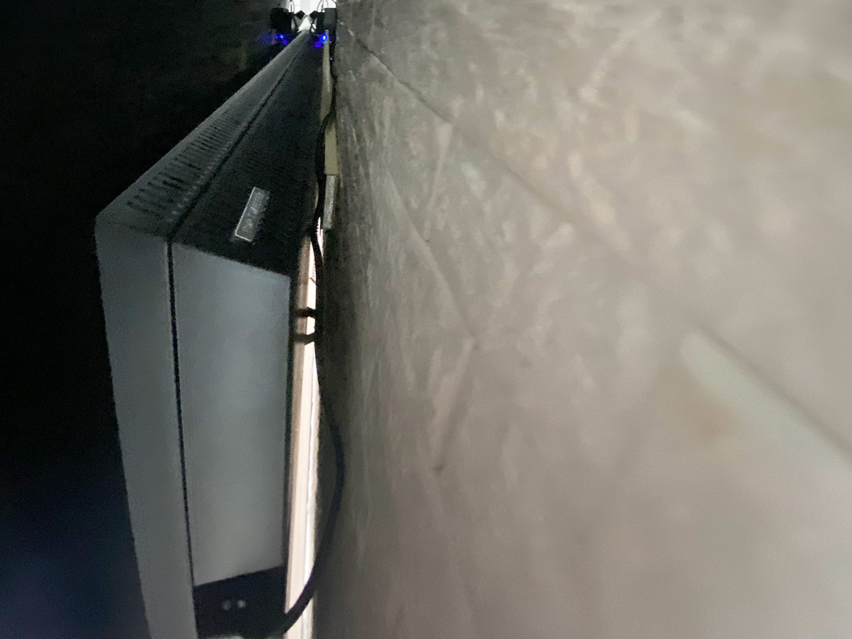 壁掛け金具は出幅の少ない角度固定式タイプ。テレビで隠れる位置にコンセントを新設。