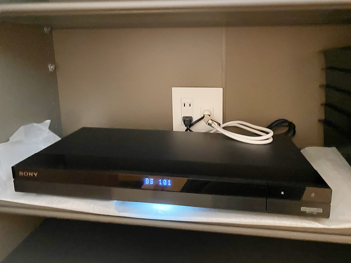 壁向こうの収納棚が用意されています。そこに設置されたレコーダー機器。背面のHDMIケーブルは壁内経由でテレビへとつながっています。