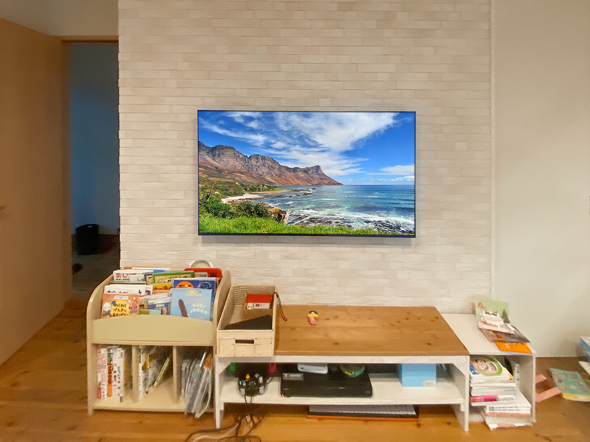 壁掛けテレビの全景写真です。テレビはK-55XR70。壁掛け時の本体サイズは横幅1225mm、高さ709mm、厚みは最大で56mm。重量は19.9kg。壁掛けしやすいモデルです。カトー電器で購入いただくと特別お値引きが適用されます。