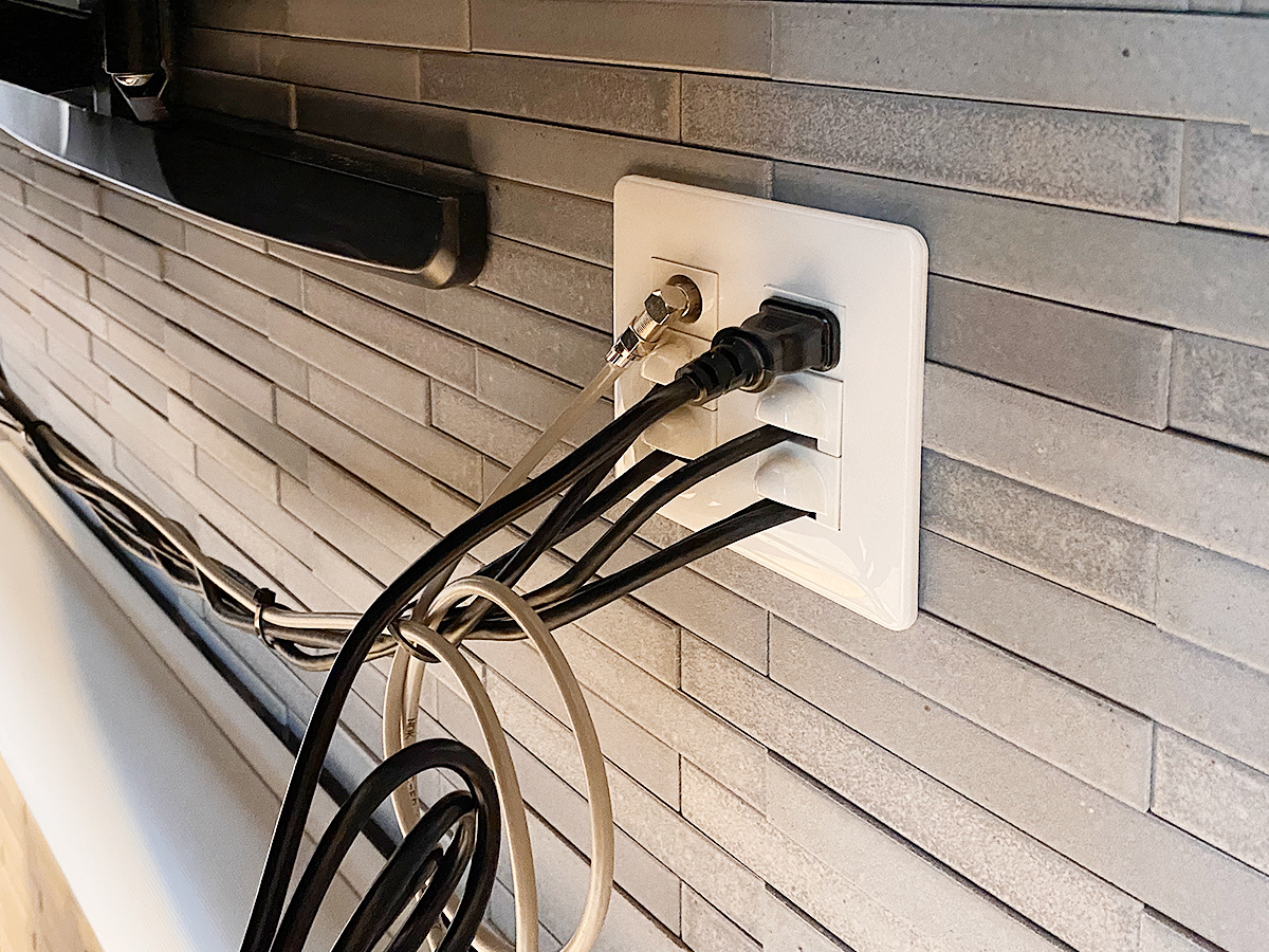 エコカラットの上から新しく設けたテレビ用専用コンセント。各種ケーブルが壁内経由で録画機器・再生機器へとつながっています。