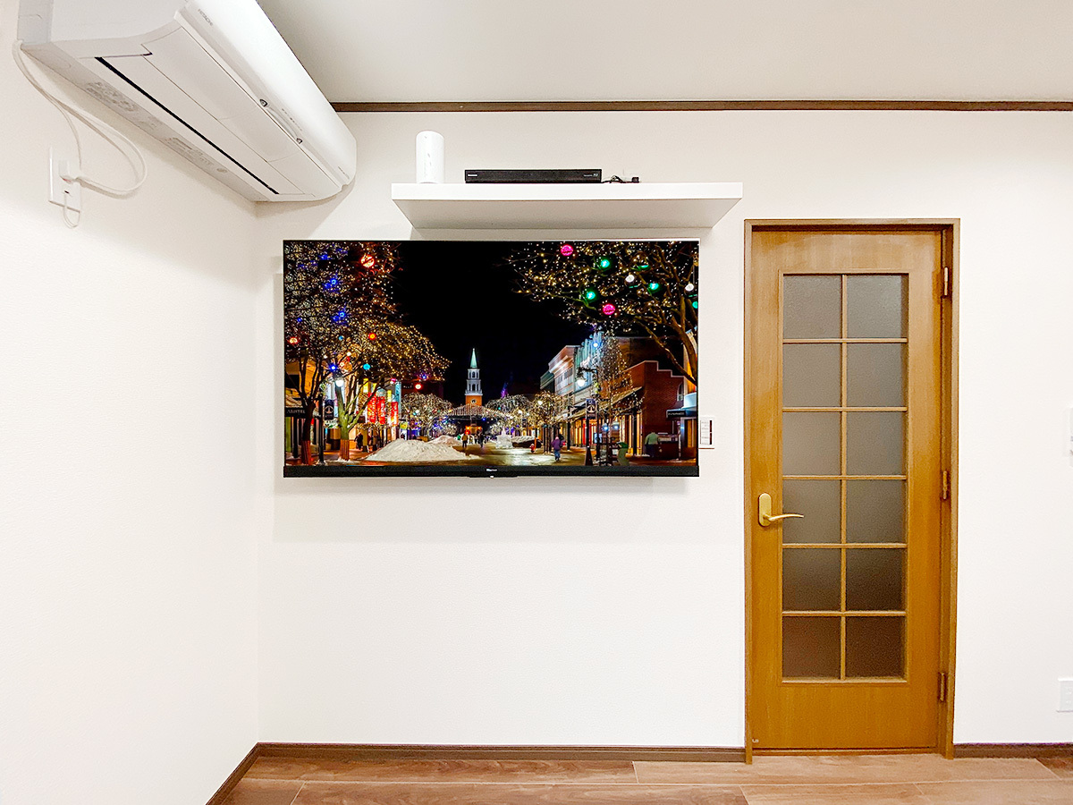 三重県桑名市でのテレビ壁掛け工事。コンセントが無い壁面に65インチテレビとウォールシェルフ(棚)を壁掛け