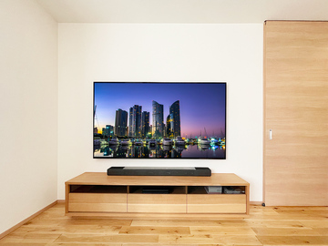 ■77インチ有機ELテレビの壁掛け
今年のソニーブラビア新モデルは70インチを超えるモデルが数多く登場し、さらなるテレビの大型を予感させてくれます。ただ70インチを超えるとさすがに大きく、お部屋の広さによっては大き過ぎると感じたり、またテレビを乗せるテレビボードの耐荷重も考えねばなりません。その点大型テレビと壁掛けの相性はよく、壁掛けにすることで視聴距離は30cmほど後退し、テレビボードの強度も考えなくてすみます。今回はそんな大型テレビの代表機種ソニーのブラビアXRJ-77A80Jの施工レポートです。

■ホームページ「無料壁掛け診断」からお問い合わせ
お客様は愛知県の一宮市在住でホームページの「無料壁掛け診断」からお部屋の現状写真をUPしてくださいました。将来壁掛けをすることを想定し「壁は補強済です」とのメッセージが添えられています。そして写真を見ると壁掛けテレビ用のコンセントパネルはありません。これはすなわちカトー電器で壁掛け工事およびテレビ用のコンセントパネル新設まで行うプランとなります。
昨今新築のお客様からのご相談で、先に壁掛けテレビ用のコンセントパネルが作られているお写真をいただく機会が増えましたが、実はこの「先駆けコンセント」が実際のテレビ位置決めの際に思わぬ障害となる場合が少なくありません。先に作られたコンセントが金具の取り付け位置と重なってしまい、仕方なく壁掛け金具（と壁掛けテレビ）の位置をずらさざる得ない…ということもありうるのです。壁掛けテレビ用のコンセントはせめてテレビと金具の種類が決まってから作っていただければ…と思います。

■その日のうちにご予約いただきました
写真とお客様のご要望を確認した施工担当者がさっそくプランとお見積もりを作成。お客様にメールにてご連絡したところ、その日のうちに施工のご予約をいただきました。(ありがとうございます)さらに
・テレビもカトー電器で購入希望
・地デジ・BSセパレーターの追加
・外付けHDDも追加
・お客様が用意したサウンドバーを取付けたい
と追加オーダーもいただき、資材部門のスタッフがテレビの発注に取り掛かりました。

■工事スタッフ お客様宅へ
施工当日は2名のスタッフが一宮市へ。お客様宅は一戸建て住宅。ちなみにハウスメーカーは住友林業さまです。ご希望の壁面を見せていただくと確かに下地補強が壁一面にしっかり行われており、77インチのテレビでも問題なく壁掛け出来ることが再確認できました。そうと分かればテレビの位置決めコンサルティングです。ブルーのマスキングテープであらかじめ調べておいたテレビの大きさの枠を作り、お客様に
「テレビの位置はどうしましょうか？」
とご相談。その結果、見た目よりも見やすさを重視し、通常よりは少し低めの位置に壁掛けすることが決まり、作業は次のステップである金具の取付へと移らせていただきました。

■壁掛け工事の基本手順
ここで壁掛けテレビ工事の大まかな流れをご紹介。
まず初めにテレビの位置決めです。
次に金具の取り付け工事。
そしてテレビで隠れる位置、更に金具の邪魔にならない位置に電源とアンテナ線を持つコンセントパネルを作ります。コンセントパネルはテレビと金具台座の位置が決まったあとです。それが新築のお宅の場合（テレビや金具のことをあまりを考慮せず？）先に作られてしまうため、主役であるテレビの壁掛けに支障をきたすという奇妙な流れが多発しています。壁掛け専門店としてこの逆転現象は何とか変えてきたいものです。
さて本件の場合は基本の手順にのっとり、スムーズに作業が進みました。テレビで隠れる位置、なおかつ金具と干渉しない良い場所にコンセントを作ることが出来、床上の既存コンセントの連携も問題ありません。
最後に77インチの有機ELテレビを箱から取り出し、慎重に壁掛け。各種ケーブルを接続し大画面の迫力ある壁掛けテレビが誕生しました。

■ここがポイント！見どころ解説
これより以下、見どころとなる各部の写真とワンポイント解説です。

thumbnail.php?id=1015_20_c8a409a135.jpg&alt=77インチの有機ELテレビを壁掛け。テレビの大型化と壁掛けは相性抜群
(↑)77インチの有機ELテレビの壁掛け工事例。テレビの大型化が進んでいますが、大型テレビと壁掛けテレビの相性は抜群です。テレビ本体が壁に取り付けられるためテレビボードの耐荷重などを考える必要もありません。

thumbnail.php?id=1015_21_64c34ca1c8.jpg&alt=テレビはソニーブラビアXRJ-77A80J。77型の有機ELテレビ
(↑)お客様のテレビはソニーのフラッグシップモデル 有機ELテレビXRJ-77A80J。カトー電器で壁掛けテレビと同時購入でお買い上げくださいました。ありがとうございます。壁掛け時の本体サイズは横幅が1722mm。高さが995mm、本体の奥行きが54mmという薄さです。重量は77インチということもあり28.9kgとかなり重め。壁掛けするには十分な強度を確保した下地が必要です。下地補強が無い壁面の場合はカトー電器が得意としている「壁内部分補強」をおすすめいたします。

thumbnail.php?id=1015_22_9e90cdb27b.jpg&alt=アンテナ線やHDMIケーブルは壁内を通す壁内配線で見た目スッキリ
(↑)一歩下がって撮影。テレビに欠かせない10ボルト電源、アンテナ線やHDMIケーブルなどはすべて壁の内側を通す「壁内配線」を採用。これによりコードなどが一切見えない壁掛けテレビが実現します。

thumbnail.php?id=1015_23_c4b82d142b.jpg&alt=77インチのサイズ感。テレビボードに置くよりも視聴距離が30cmほど後退します
(↑)77インチテレビのサイズ感をご確認ください。テレビボードの上に置いた場合はこれより30cmほど手前にせり出す感じになります。この30cmの違いのため、壁掛けを機に一回り大きいテレビに買い替えられる方もいらっしゃいます。

thumbnail.php?id=1015_24_aed0daa13a.jpg&alt=側面。XRJ-77A80Jの薄さが実感できます
(↑)恒例の壁掛け側面の様子。下地補強が壁の内部で行われているため、壁面と金具が直接接しています。また角度固定式タイプの金具を使うことでXRJ-77A80Jの本体の薄さがより強調されています。

thumbnail.php?id=1015_25_4b3a6adab0.jpg&alt=今回はテレビボードとの併用。サウンドバーも据え置きです
(↑)お客様は壁掛けテレビとテレビボードを併用。サウンドバーの置き場もテレビボードの上となりました。テレビボードを無くす場合はサウンドバーは「壁掛け」「棚を設置してその上に」といった選択肢が考えられます。

thumbnail.php?id=1015_26_9fba36f7ca.jpg&alt=工事中の写真。金具台座を取り付け。床上コンセント電気工事士の資格を持つスタッフが一度取り出し配線の組み替え作業中
(↑)工事途中の写真も紹介しておきましょう。壁面のマスキングテープは訪問直後に行われたテレビの位置決めによって作られたもの。その下の水平ラインはテレビボードの上辺ラインです。その下では電気工事士の資格を持つスタッフが既存のコンセントを一旦取り出し、配線の組み換え作業を行っています。
青い枠の中では壁掛け金具の台座が水平に取り付けられています。

thumbnail.php?id=1015_27_63c1af1806.jpg&alt=テレビの位置が決まり、金具の取付が終わって初めてコンセントパネルの位置が決まります
(↑)テレビの位置が決まり、金具の取付が終わって初めてコンセントパネルの新設に入れます。金具と干渉せず、しかもテレビの枠からはみ出さない場所、なおかつ既存のコンセントから延長しやすい場所として今回は金具の斜め下にコンセントを作ることにしました。

thumbnail.php?id=1015_28_802faa3f4e.jpg&alt=今回は金具の斜め下。既存コンセントのほぼ真上になりました。
(↑)写真の壁掛け金具はカトー電器オリジナル商品です。壁掛けテレビ専門店として培ったノウハウや工夫が多数詰め込まれています。

■大型テレビへの買い替えを機に壁掛けもご検討ください
より鮮やかな有機ELテレビや一回り大きいテレビなど、テレビの買い替えをお考えでしたら是非壁掛けもご検討ください。カトー電器にご相談くだされば送っていただいた写真とリクエストをベースにお客様にとって最適なプランをご提案させていただきます。
