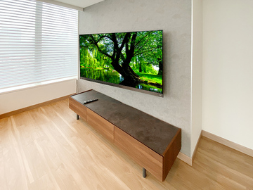 ■壁掛けテレビと同時に壁紙クロスの貼り替えも
カトー電器商会ではテレビの壁掛けとセットで壁紙クロスの貼り替え工事も受け付けております。
「壁紙の汚れが目立ってきた」
「壁紙を変えてお部屋の雰囲気を一新したい」
などテレビ壁掛けを機会に壁紙も貼り替えたい方はカトー電器商会にご相談ください。
・壁内補強工事
・壁内配線工事
・クロス貼り替え工事
・テレビの壁掛け工事
これらの作業を一日で行い、夕方には完成させてしまいます。

■大阪市からお問い合わせ
今回の施工例は大阪市のお客様。マンションにお住まいで弊社ホームページの「無料壁掛け診断」からお部屋の写真をUPしてくださいました。写真を見ると赤い枠線でテレビの位置が描かれており、お客様の壁掛けに対する思いが伝わってきます。さっそく工事スタッフが詳細なプランとお見積もりを作成し、お客様にご連絡。クロスの品番決めなど何度かメールをやり取りし、正式なご予約をいただきました。

施工当日はクロス担当のスタッフも含め、3名が名古屋から大阪市へ。
まずは正式なテレビの位置決めをお客様とおこない、既存のクロスをはがすところからスタート。今回の壁面は壁掛けを想定しておらず下地補強が施されていないため、この時点で壁内部分補強の工事、および配線ルートの確保を済ませておきます。電気工事士の資格を持つスタッフが既存コンセントを分解し、100ボルトの電源やアンテナ線を手際よく新しく作られたコンセントに通していきます。
下地準備が終わったら、新しい壁紙を貼っていきます。今回使用した壁紙はサンゲツ社のアクセントクロス「FE74174」です。
https://www.sangetsu.co.jp/product/detail/FE74174/
新しい壁紙が貼られたたら可動式タイプの金具を設置し、コンセントパネルも仕上げていきます。壁掛けテレビの工事の工事前や工事後に壁紙を張り替えると金具やコンセントの処理に悩みますが、同時に行えばこれらの処理は驚くほどスムーズに進みます。
最後にお客様ご用意の65インチ液晶テレビを取り付け、各種ケーブルを接続すれば工事完了。アクセントクロスを背景にした大型壁掛けテレビが誕生しました。

■各部の見どころを解説
これより以下、各部の写真と見どころ解説です。

thumbnail.php?id=1134_18_8f9c53a744.jpg&alt=大阪市のマンションで壁紙クロスを貼り替えたあとに65インチ液晶テレビを壁掛け
(↑)大阪市のマンションで壁紙クロスを貼り替え、65インチの液晶テレビを壁掛けしました。壁掛けテレビとクロスの貼り替え。同時に行えば工事は一日で完了します。

thumbnail.php?id=1134_19_2e5720507d.jpg&alt=テレビは東芝レグザ65Z740XS
テレビは東芝レグザの65Z740XS。お客様がご用意くださいました。壁掛け時の本体サイズは横幅が1453mm、高さが866mm、本体の厚みは91mmです。スタンドを外した重量は26.4kg。金具の重量もありますので壁面にはしっかりとした強度が求められます。

thumbnail.php?id=1134_20_5312403c1c.jpg&alt=壁掛け金具は上下左右に角度が変えられる可動式金具。テレビ用のコンセントは新しく作りました
(↑)金具は上下左右に角度が変えられる可動式タイプです。写真は金具を動かした背面の様子。新しく作られたテレビ用コンセントに各種ケーブル類がつながっているのがお分かりいただけると思います。

thumbnail.php?id=1134_21_3b29af53a7.jpg&alt=新しい壁紙と既存の壁紙の境界線には見切り材を貼っています。
(↑)新しく貼られた壁紙はサンゲツ社のアクセントクロス。既存の壁紙と接する箇所にはお客様リクエストにて見切り材を用いています。

thumbnail.php?id=1134_22_9fcafa961d.jpg&alt=お客様から送っていただいた写真画像。赤い枠もお客様によるものです。
(↑)ホームページ「無料壁掛け診断」からお客様がUPしてくださった壁面写真。テレビの位置をし示す赤い枠線も入っています。このように
「ここに壁掛けしたいです！」
とお客様の思い、本気度が伝わってくる写真は担当スタッフを奮い立たせます。


■壁紙もリニューアルしませんか？
経年変化やお子さんのお絵描き（子どもはどうしてあんなに壁に絵を描きたがるのか…）などで壁紙の貼り替えをお考えの方へ。壁紙と一緒にテレビ本体を壁掛けにしてみませんか？壁紙の種類はサンゲツのホームページから自由に選んでいただき、品番をご指名くだされば施工当日スタッフがご自宅までクロス壁紙を持参します。
ご相談やお問い合わせはお電話、もしくはホームページの無料壁掛け診断からどうぞ。壁紙クロスの他にもエコカラット同時施工も受け付けております。
