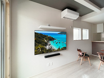 ■カトー電器ではソニー、シャープのテレビも販売中
カトー電器商会では壁掛け工事と一緒にソニーのブラビアシリーズ、シャープのアクオスシリーズを取り扱い・販売しております。新機種が登場すると壁掛けテレビのテスト(テレビ背面のチェックや金具との相性などを確かめます)をおこない、注意点やポイントなどを社内で共有。確実かつ手際よく壁掛けできる工法を日々追究しています。
壁掛け工事とセットでテレビをご購入いただくとテレビには特別お値引きが適用され、施工当日にテレビも一緒にお届け…という流れになります。工事日まで巨大な段ボールがリビングを占有するようなことはなく、工事が完了したら段ボールや梱包材などは弊社が責任をもって回収いたします。
その日のうちに新品のテレビが届き、壁掛けまで完了するのが「テレビ同時購入壁掛け」です。弊社ホームページ「無料壁掛け診断」からテレビ同時購入も選べますので、どのお店で購入すべきはお悩みの方は是非一度お見積もりご相談ください。

■テレビとサウンドバー、シェルフ(棚)の壁掛け
今回ご紹介する施工例もテレビ同時購入の案件です。お客様はカトー電器のホームページ「無料壁掛け診断」からお部屋の写真をUPしてくださいました。写真を見ると床上にテレビ用コンセントが用意されており、壁内を垂直に配線すればケーブルが見えない壁掛けテレビが実現しそうです。さっそく担当者がプランを作成し概算のお見積もりをお客様にメールでご連絡。お客様も納得され、工事ご依頼のご予約をいただきました。(ありがとうございます)
施工当日。スタッフ2名がテレビと一緒にお客様宅をご訪問。ご挨拶の後、お客様と一緒にテレビ、サウンドバー、それにシェルフの位置決め相談。それぞれの設置場所が決まれば工事スタートです。まずは床上のコンセントを一旦分解し、壁内の様子を確認。ここを起点に100ボルトの電源やアンテナ線などを壁内に配線してゆきます。
壁内の調査で壁掛け用の補強が施されていることが分かりましたので、各自配線工事と壁掛け金具、シェルフの取り付けに専念していきます。
角度固定式の金具を取り付け、テレビで隠れる位置にコンセントパネルを新設。
テレビ上にはウォールシェルフを設置。こちらも目立たない位置にコンセントパネルを作ります。テレビ下にはサウンドバー用の配線ルートを設け、サウンドバーを設置します。
最後に持ち込んだ新品のテレビ本体を開梱・壁掛けしたら工事は完了です。
ほぼ半日で何もなかった壁面に、65インチの大画面壁掛けテレビとサウンドバー、ウォールシェルフが誕生しました。

■各部の写真と見どころポイントの解説
以下、各部の写真と見どころポイントの解説です。シェルフ側のコンセントにはHDMI端子が組み込まれており、ここにレコーダー機器などを接続するとテレビにさ出力されるようになっています。

thumbnail.php?id=890_20_050bf8a519.jpg&alt=名古屋市で65インチ液晶テレビとサウンドバー、ウォールシェルフを壁掛け
(↑)名古屋市で65インチ液晶テレビとサウンドバー、さらにウォールシェルフ(棚)の壁掛け施工です。ケーブル類は目立たぬように壁の内側を通す「壁内配線」となっています。テレビ周りに黒いコード類が見えないのが特長です。

thumbnail.php?id=890_21_48734f37fe.jpg&alt=テレビはカトー電器で同時購入していただいたブラビアKJ-65X9500H
(↑)テレビはカトー電器で同時購入していただいたソニーのブラビア KJ-65X9500H。65インチの液晶テレビ。壁掛け時の本体サイズは横幅が1448mm、高さが833mm、本体の厚みは70mmになります。

thumbnail.php?id=890_22_890a3d1e69.jpg&alt=テレビ上にはウォールシェルフ、テレビ下にはサウンドバー名という組み合わせ
(↑)テレビ上にウォールシェルフ、テレビ下にサウンドバー、テレビ背面に録画用ハードディスクという組み合わせです。テレビを中心に音響も録画も楽しめる構成となっています。

thumbnail.php?id=890_23_dd83700fa6.jpg&alt=ウォールシェルフには将来セットアップボックスが置かれる予定です
(↑)ウォールシェルフには将来セットアップボックスが置かれる予定です。あまりさわるものでなければ、ウォールシェルフはテレビ上でも特に問題ありません。

thumbnail.php?id=890_24_f4da7d4c09.jpg&alt=シェルフ側の新設コンセントにはテレビとつながるHDMI端子を組み込みました。
(↑)シェルフ側のコンセントパネルには壁内経由でテレビとつながるHDMI端子を一つ組み込んであります。

thumbnail.php?id=890_25_8e898333d3.jpg&alt=シェルフ側のコンセント。左列中央がHDMI端子
(↑)シェルフ側コンセントの正面写真。左列中央がHDMI端子です。ここに各種機器を接続すればテレビに映像やサウンドを出力したり、テレビ番組を録画できたりします。

thumbnail.php?id=890_26_3b38ef9fa9.jpg&alt=側面から。テレビの後ろには録画用の小型ハードディスクが設置されています。
(↑)側面から撮影。テレビの後ろには空きスペースを利用して録画用のハードディスクを設置しています。

thumbnail.php?id=890_27_75d0cd898e.jpg&alt=工事開始直後の様子。この壁面にテレビ用とシェルフ用にコンセントが2つ新しく作られることになります。
(↑)工事開始直後の様子。こちらの壁面にテレビ用とシェルフ用のコンセント2つが新たに作られました。床上コンセントは分解し、壁内の調査が始まろうとしています。


■床に何も置きたくない方へ
ルンバなどをお持ちで床に何も置きたくなければ、壁掛けテレビ＋ウォールシェルフの組み合わせが便利です。レコーダーやゲーム機などをシェルフに置き、壁内配線でテレビと接続すれば床まわりはいつもスッキリ。さらに床上のHDMIコンセントパネルを新設すれば、ゲーム機などを「遊ぶ時だけ使う」「遊び終わったら所定に場所に片づける」といった習慣が生まれます。とりわけプレステなどのように筐体の大きなゲーム機をお持ちの方には有効です。
テレビ周りにものが散乱しがちであったり、テレビボードが思いのほか場所を取っている方は、是非ご検討ください。
ご相談・お問い合わせは弊社ホームページの「無料壁掛け診断」からどうぞ。
