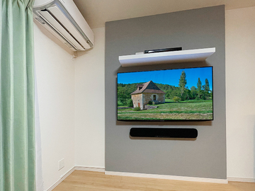 ■千葉県松戸市からのご相談
お客様は千葉県にお住まいでカトー電器のホームページ「PIXY無料設置相談」からお問い合わせくださいました。壁の現状写真と一緒に添えられたメッセージ
「床から天井までの高さは240cmです。この写真の壁にフェイクウォール「PIXY」を設置し、55インチのテレビを1台取り付けることは可能でしょうか？また棚とサウンドバーの設置も予算に合えば行いたいです。おおよその金額も教えてください。」
わざわざ天井までの高さを測ってくださりありがとうございます。施工担当者がさっそく施工費などを計算。これまでの施工写真と一緒にお見積もりをお客様にメールで送信。
何度かメールでやり取りし、正式に工事のご依頼をいただきました。(ありがとうございます)

■千葉県への出張工事
施工当日。スタッフ2名が名古屋から千葉県へ。お客様宅は戸建住宅。ハウスメーカーは飯田産業様です。
まずは壁の要素を見せてもらいます。写真で見せていただいた通りの壁です。問題なく設置出来ることが確認できましたので、お客様と一緒にテレビの位置決めをおこないます。今回はテレビ上にウォールシェルフ(棚)、テレビ下にサウンドバーを設置しますので全体のバランスも考えねばなりません。テレビの位置が決まったらいよいよ工事開始です。
各種部材をお部屋に運び込み、高さ2400mm、幅1620mmのPIXY本体を組み立て設置していきます。今回の外装はサンゲツの壁紙クロス。グレーの落ち着いたトーンが特徴的です。
同時進行でPIXY内部に電源やアンテナ線も通していきます。ご希望の壁面にはコンセントが無いため、90度対角壁のコンセントから100ボルト電源とアンテナ線を延長しました。
テレビで隠れる位置に、そして棚の位置にコンセントをそれぞれ新設。壁掛け金具は角度固定式タイプ。お客様ご用意のテレビを壁掛けし、更にシェルフ、そしてサウンドバーを設置してゆきます。午前中から始めた工事が夕方には完了。写真のようにお部屋の一角に別空間ともいえる壁掛けテレビが誕生しました。

■各部の写真と見どころポイント
以下、各部の写真と見どころポイントの解説です。テレビのみならず、ウォールシェフル、サウンドバーのオプションも盛り込んだ姿にご注目ください。

thumbnail.php?id=989_30_5400e7305b.jpg&alt=千葉県松戸市でフェイクウォールPIXYを設置し、55インチテレビを壁掛け
(↑)千葉県松戸市でフェイクウォールPIXYを設置し、55インチテレビを壁掛けしました。テレビ上にウォールシェルフ(棚)、テレビ下にはサウンドバーも壁掛け。

thumbnail.php?id=989_31_43b931d008.jpg&alt=テレビはシャープのアクオス有機ELテレビ4T-C55CQ1
(↑)テレビはシャープのアクオス有機ELテレビ4T-C55CQ1。55インチの有機ELテレビです。壁掛け時のサイズは横幅ga1228mm、高さは721mm、厚みは最大で59mm。

thumbnail.php?id=989_32_451f7214b8.jpg&alt=テレビ上にはレコーダー置き場としてウォールシェルフと設置。専用コンセントもついています。
(↑)テレビ上にはレコーダー置き場としてウォールシェルフも設置しました。こちらにも専用コンセントもついています。

thumbnail.php?id=989_33_a8748a477a.jpg&alt=シェルフのコンセントには予備のHDMIケーブルもご用意。
(↑)シェルフのコンセントには予備のHDMIケーブルを用意。将来ゲーム機などが増えてもここに設置・接続すればテレビに映像とサウンドが出力されます。

thumbnail.php?id=989_34_74cdc53461.jpg&alt=テレビ下にはサウンドバーを壁掛けしました。配線はPIXY内部を通しています。
(↑)テレビ下にはサウンドバーを壁掛けしました。各種配線はPIXY内部を経由しており、コード類が見えないところがポイントです。

thumbnail.php?id=989_35_3424bf8a99.jpg&alt=足元は巾木(はばき)を使って見映えよく仕上げています。
(↑)足元は巾木(はばき)を使い、既存の壁と統一感を出し、かつ見映えよく仕上げています。

thumbnail.php?id=989_36_948db59ad4.jpg&alt=壁掛け金具は角度固定式タイプを採用。
(↑)壁掛け金具は角度固定式タイプを採用しました。テレビの出幅を抑えたい方には角度固定式の金具がおすすめです。

thumbnail.php?id=989_37_ac7686d369.jpg&alt=ウォールシェルフとテレビ、テレビとサウンドバーの間にはスペースを空け、遠目で見た際のバランスを整えています。
(↑)ウォールシェルフとテレビ、テレビとサウンドバーの間にはそれぞれスペースを空けて遠目で見た際のバランスを整えています。

thumbnail.php?id=989_38_46c07c9289.jpg&alt=こちらは工事前にお客様が送ってくださった現状写真。コンセントが無く、左側の壁面にコンセントがあることが確認できました
(↑)こちらは工事前にお客様が送ってくださった現状写真。コンセントが無く、左側の壁面にコンセントがあることが確認できました

thumbnail.php?id=989_39_d16bd8549f.jpg&alt=工事前と工事後の比較画像です。
(↑)工事前と工事後の比較画像です。雰囲気が一新されたのがお分かりいただけると思います。


■関東、関西にも施工でお伺いします
フェイクウォールPIXYはカトー電器のオリジナル商品。カトー電器のスタッフが関東から関西まで直接お伺いし、施工を担当いたします。本作のようにコンセントが無い壁面であっても90度対角壁から目立たず延長するなどして設置することもできますので、興味のある方はどうぞお気軽にご質問・お問い合わせください。「賃貸なので壁に穴を開けられない」という方からはもちろん、「新築だから壁に穴を開けたくない」という方からも多くのご相談をいただいております。
本物の壁に代わって、さまざまな工事が大胆にできるのがPIXYのウリですので、棚やサウンドバー、HDMIコンセントなど、ぜひあなたも「欲張った」プランを考えてみてください。